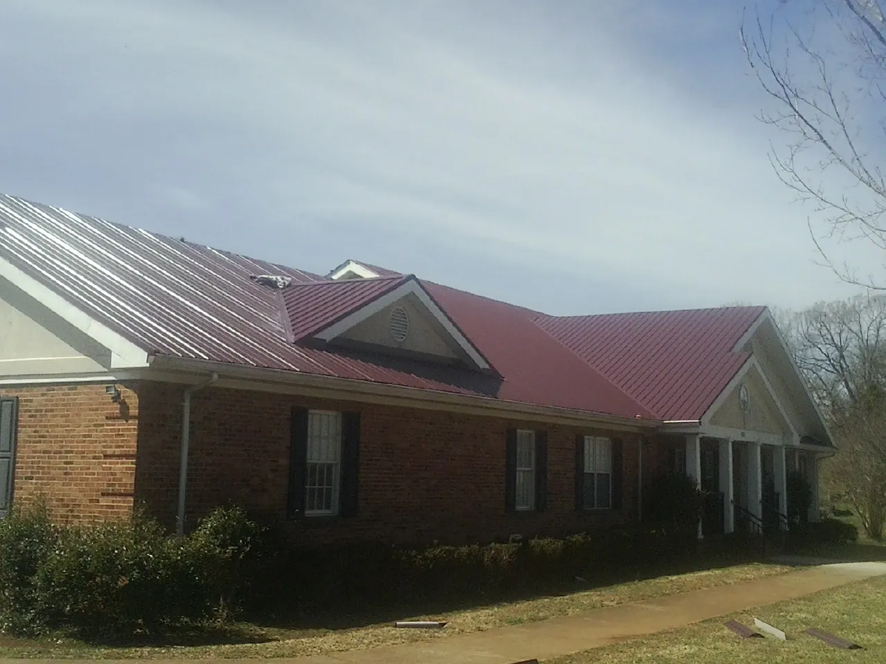 Red metal roof with gabled entries on a long brick building, from a Hail Damage Roof Repair job in Simms