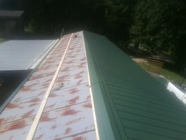 Old rusted panels beside newly installed green metal roofing — Wind Damage Roof Repair by Roofing Brothers in Simms