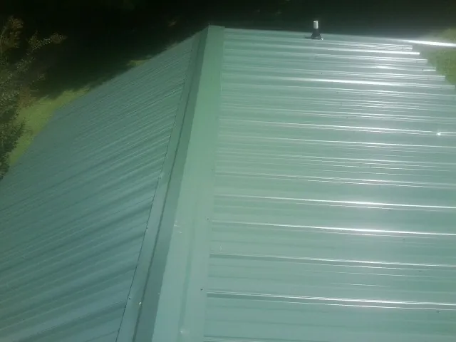 New green metal panels meeting at the ridge of a roof — Flat Roof Repair work by our crew in Simms