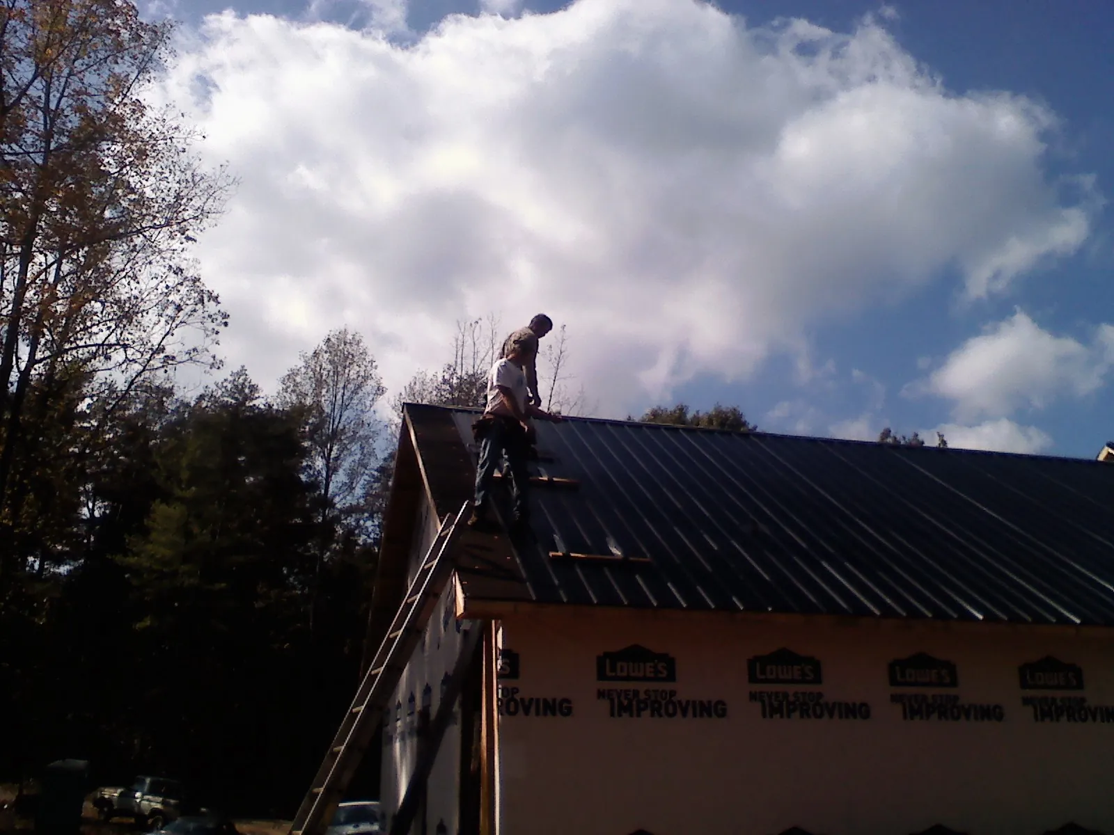 Roofer fastening dark metal panels high against a cloudy sky, from a Roof Inspection job in Simms