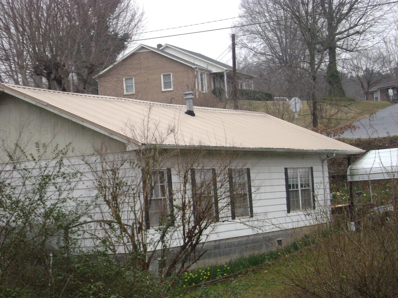 Tan metal roof on a white sided house set into a hillside — Commercial Roofing by Roofing Brothers in Simms