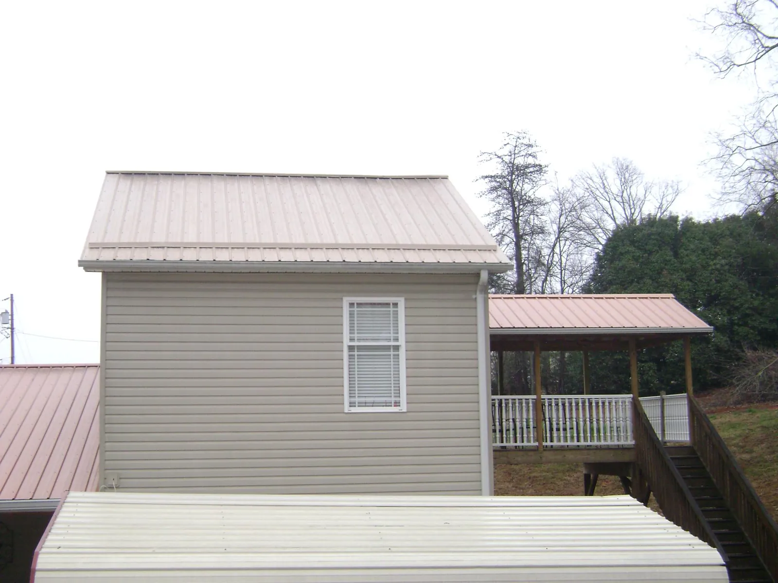 Tan metal roofs on a two story addition and attached porch, from a Roof Replacement job in Simms